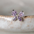A silver butterfly stud earring with four faceted light purple gemstones, resting on a textured white ceramic surface.